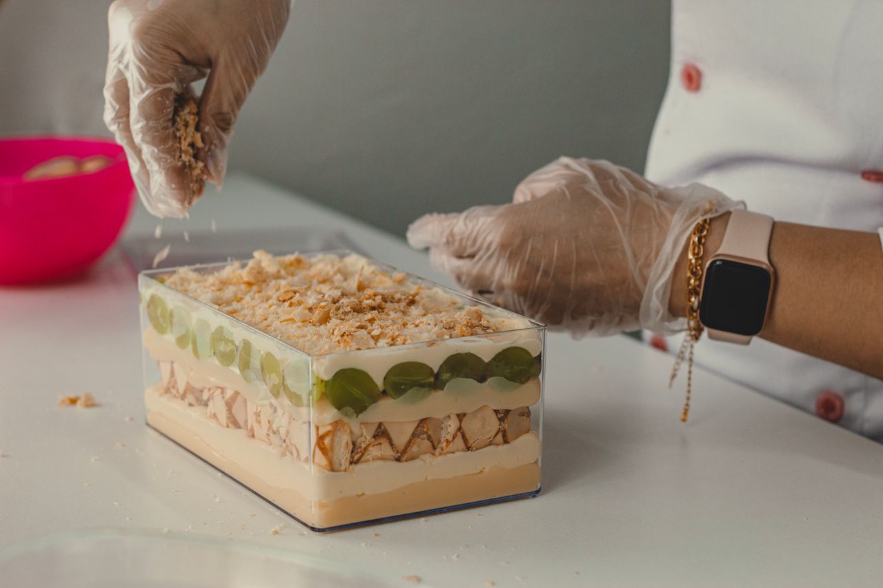 A person wearing gloves carefully prepares a layered dessert.