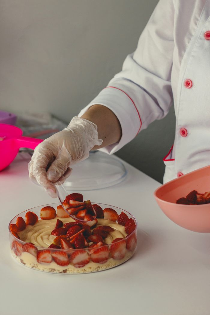 Chef skillfully decorates a strawberry cake in a professional kitchen setting, showcasing culinary art.