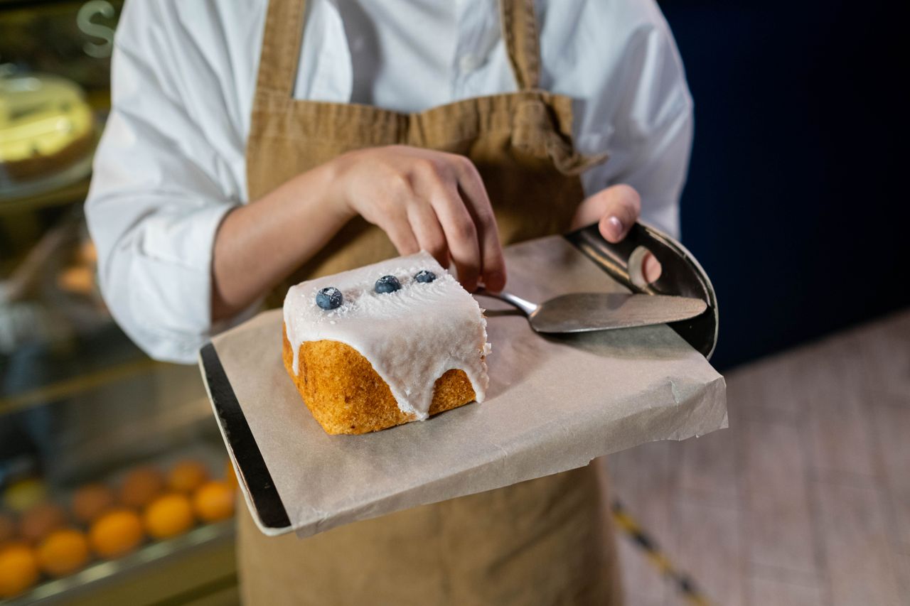 Close-up of a baker icing a delicious blueberry cake in a modern bakery setting.